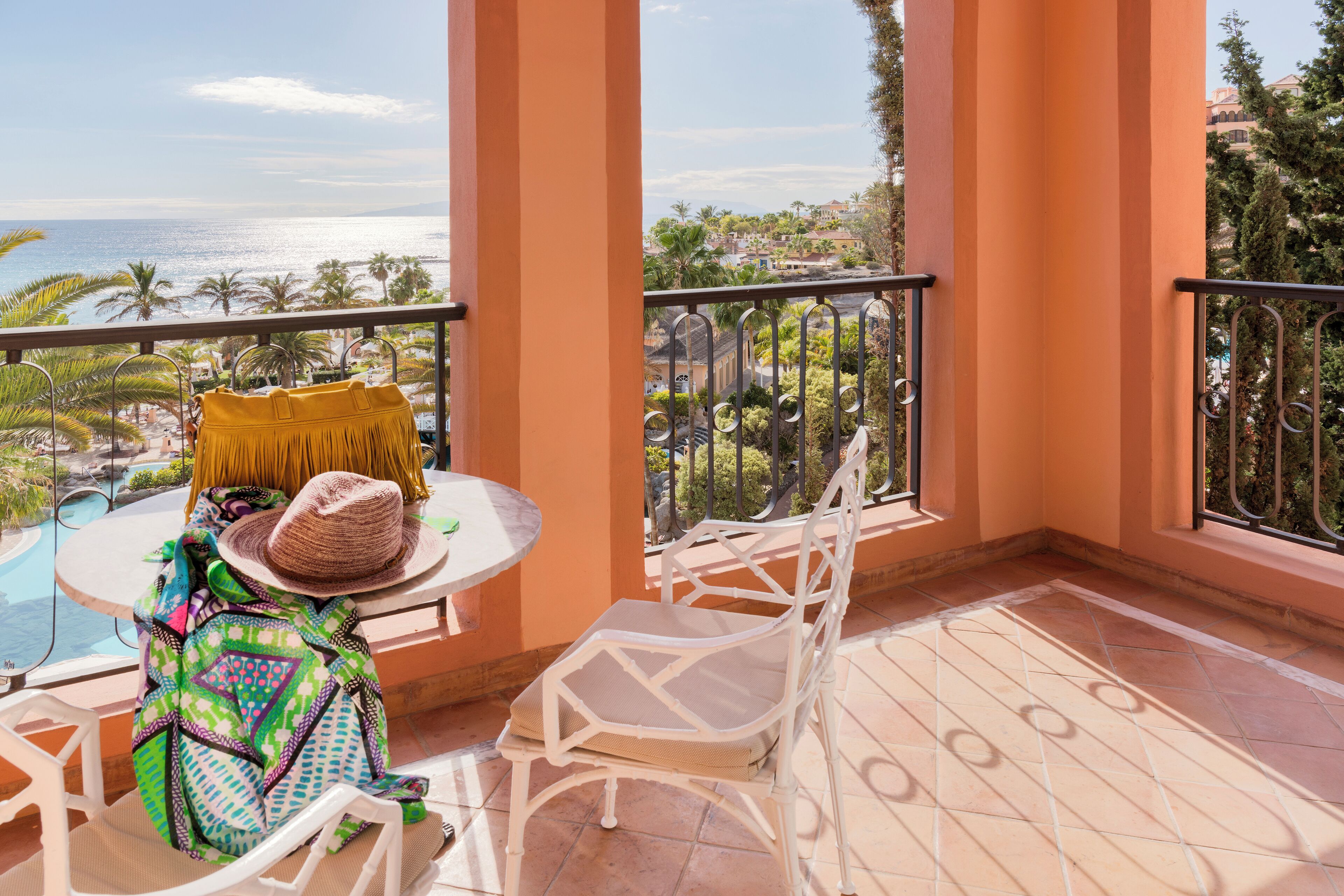 A balcony with a view of the ocean, a pool, and palm trees.