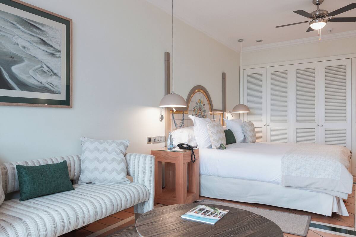 A hotel room with a sofa, a bed, a nightstand, a lamp, and a ceiling fan.