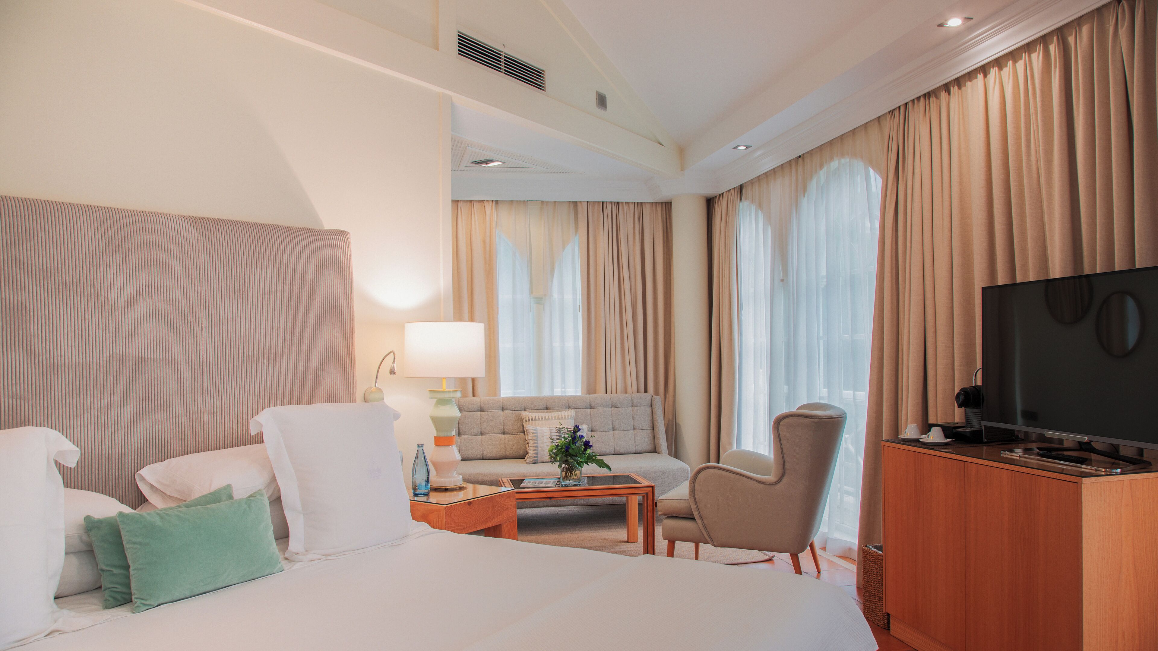 Une chambre d’hôtel avec un lit, un canapé, une table basse, une télévision et des rideaux.