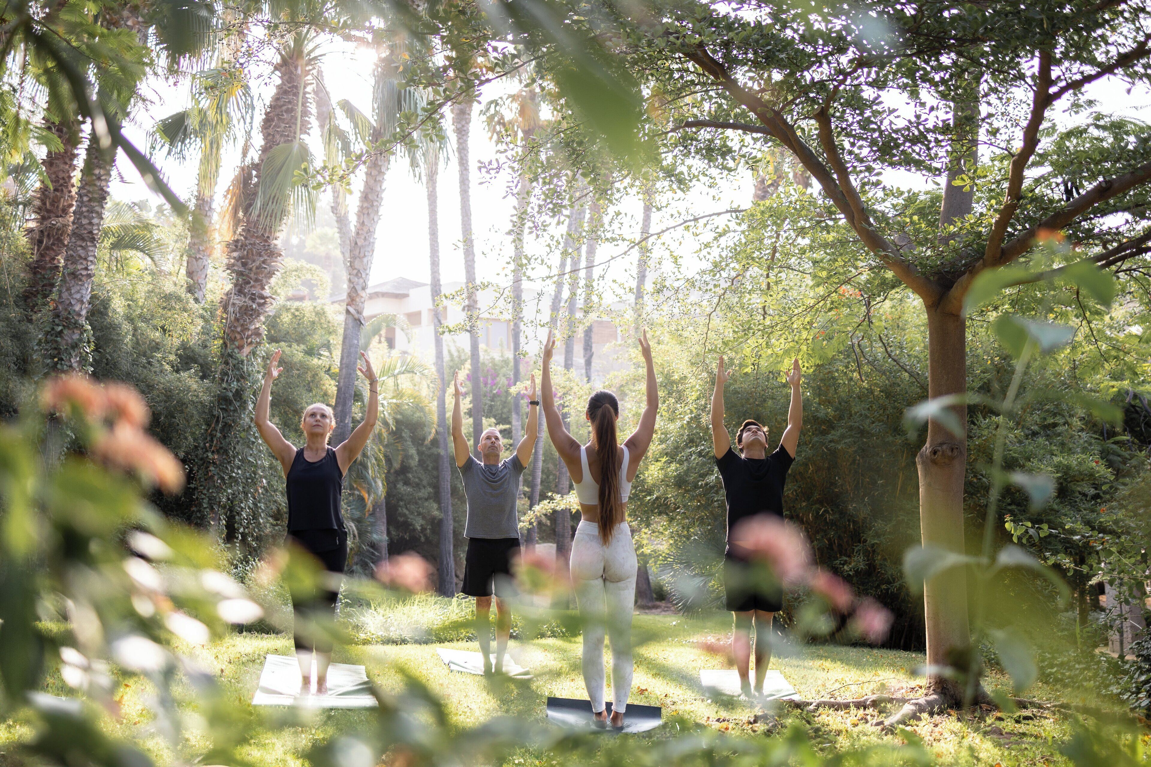 A group of people practicing yoga outdoors in a natural setting with trees and greenery.