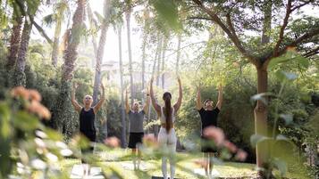 A group of people practicing yoga outdoors in a natural setting with trees and greenery.
