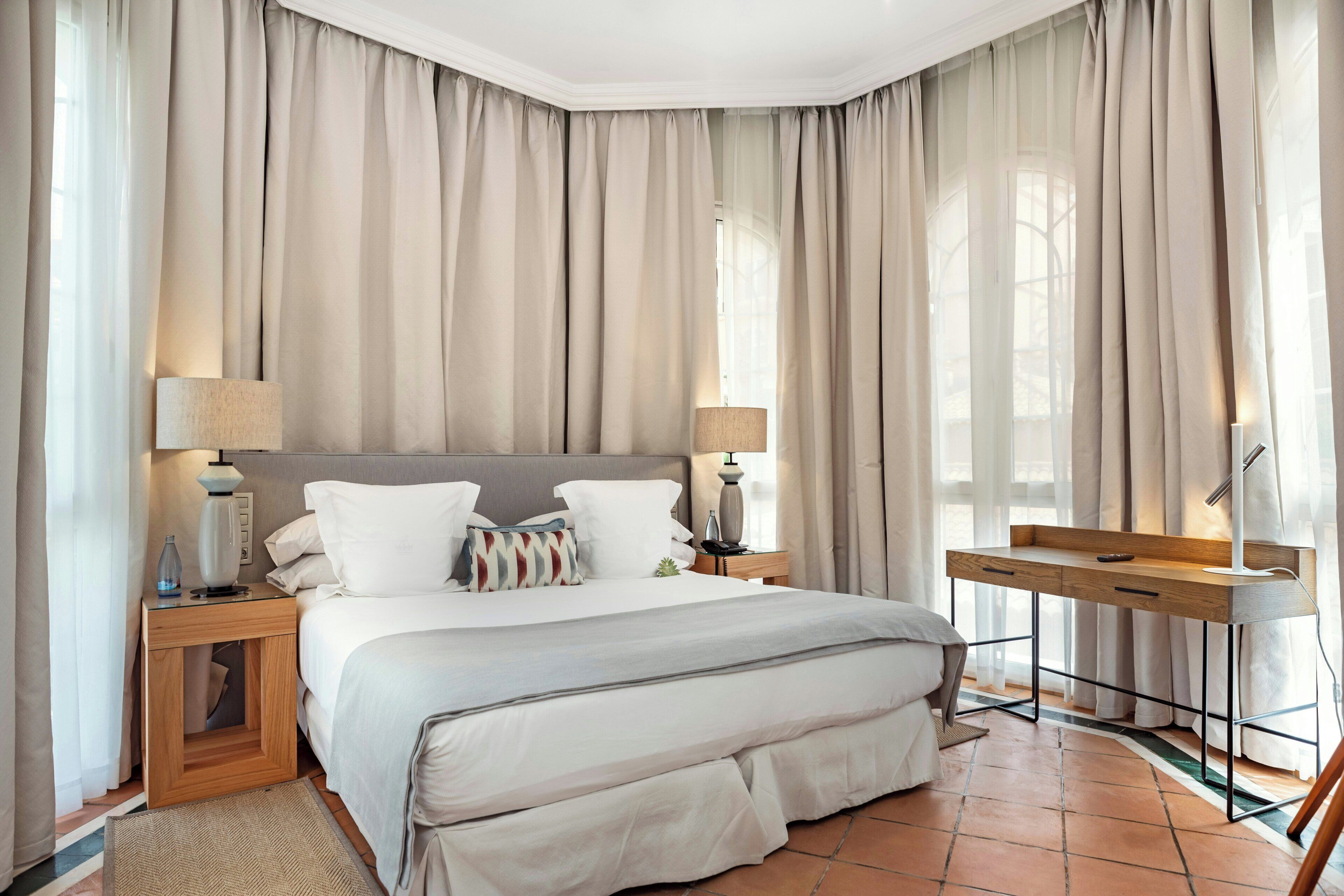 Een slaapkamer met een bed, nachtkastjes, een bureau en gordijnen.