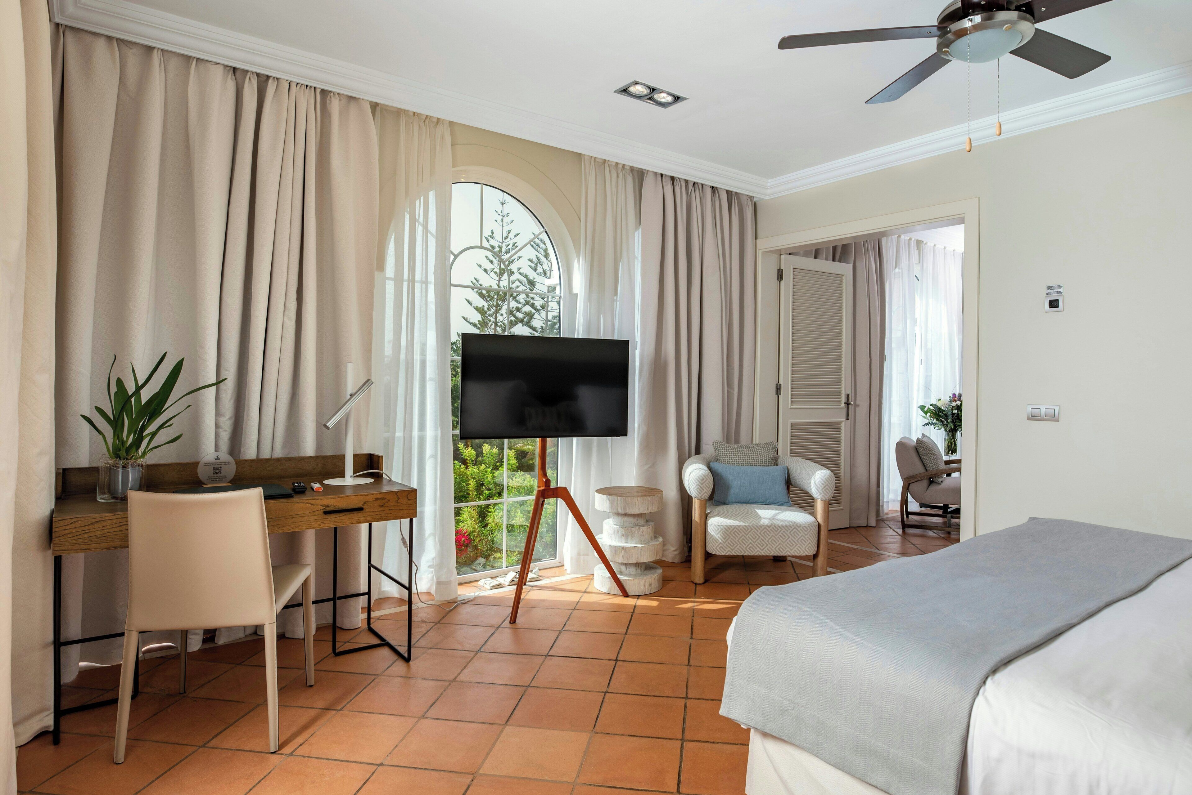 Une chambre d’hôtel avec un lit, un bureau avec une télévision, une chaise et une vue sur la verdure.