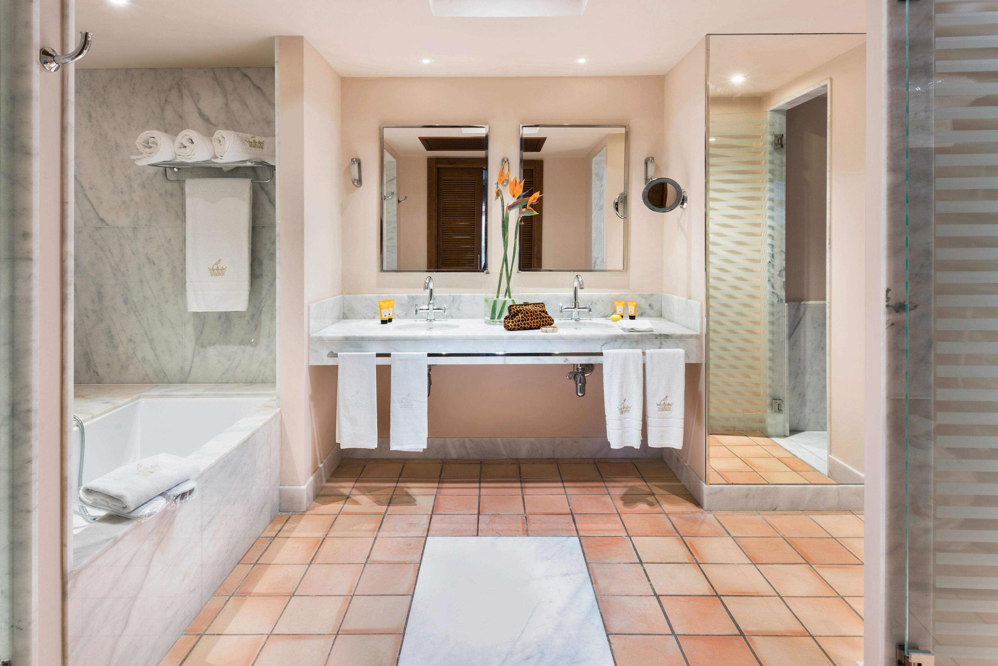 Un baño moderno con lavamanos de mármol, espejos dobles, ducha con puerta de cristal y suelo de baldosas.