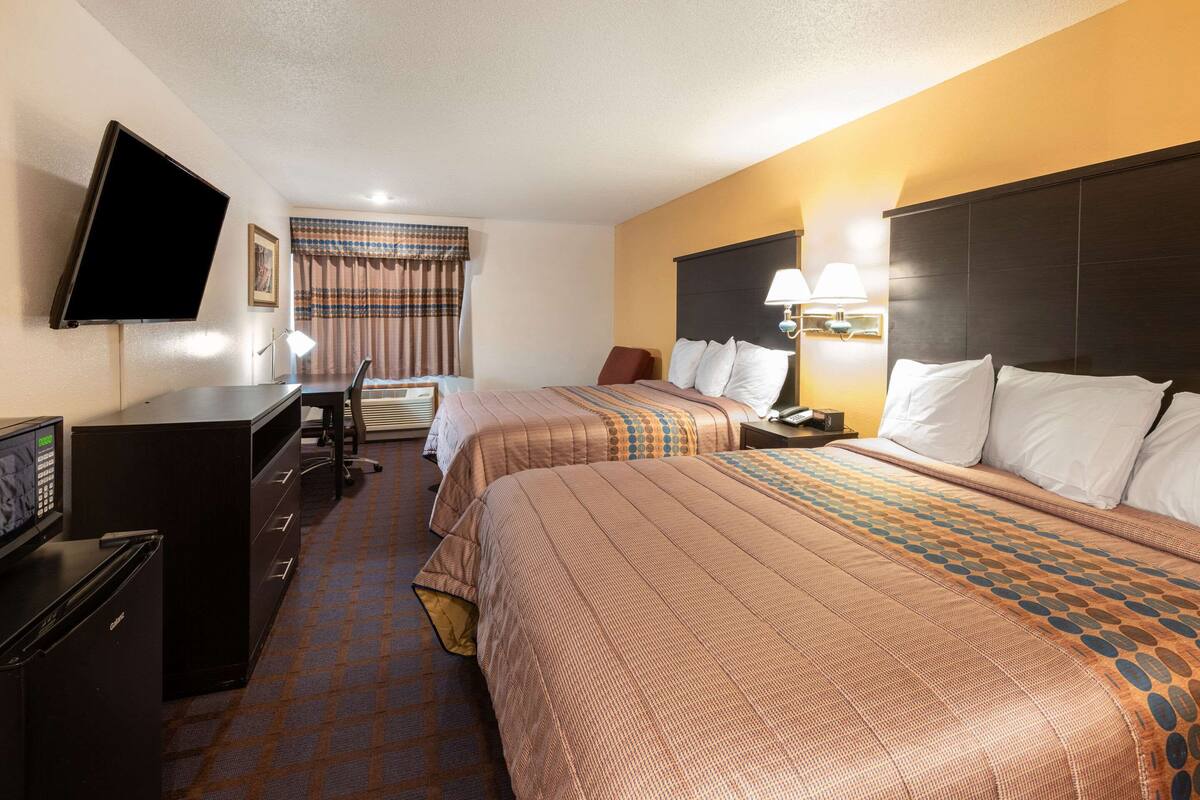A hotel room with two beds, a desk, a television, and a desk lamp.