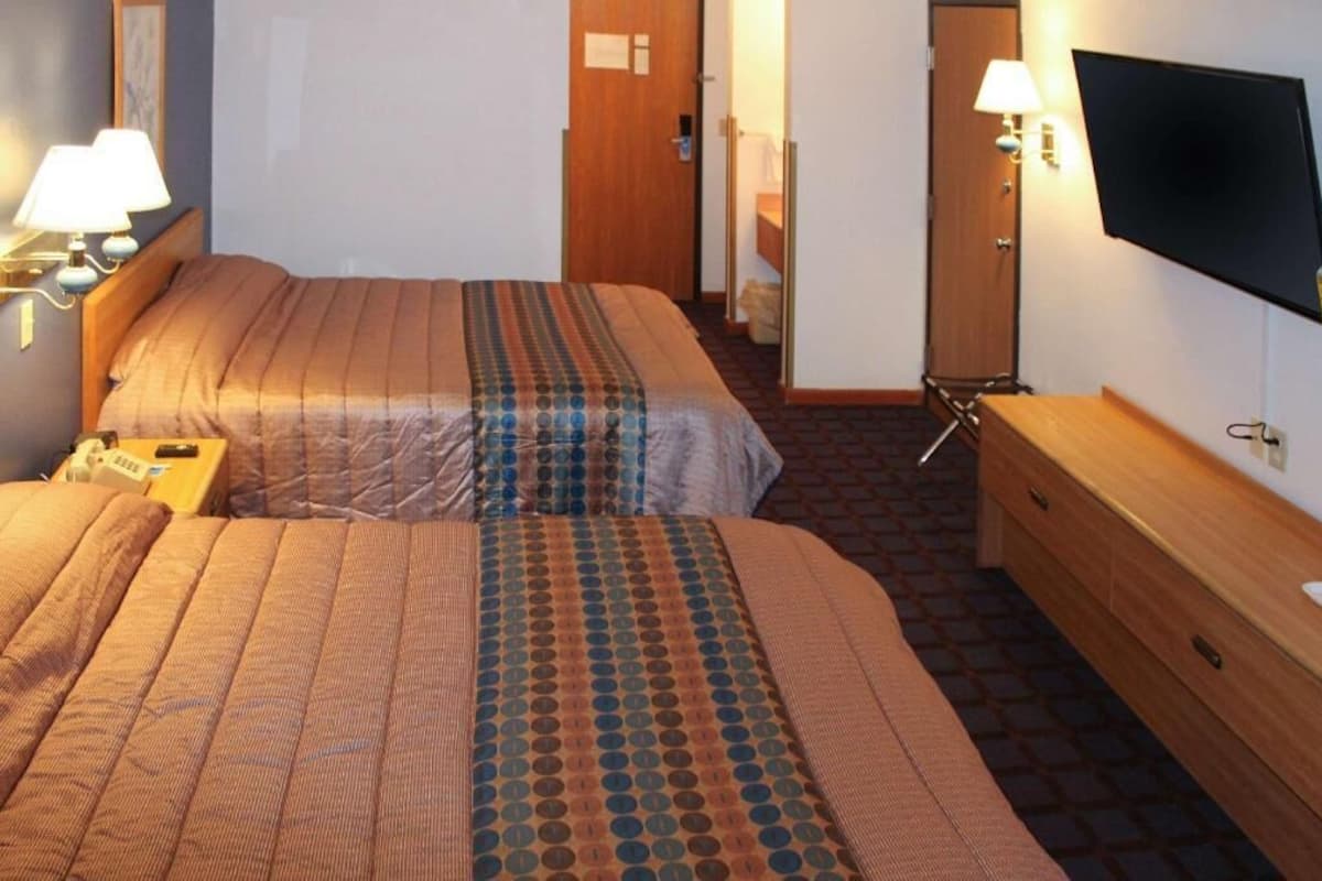 A hotel room with two beds, a TV, a desk, and a mirror.