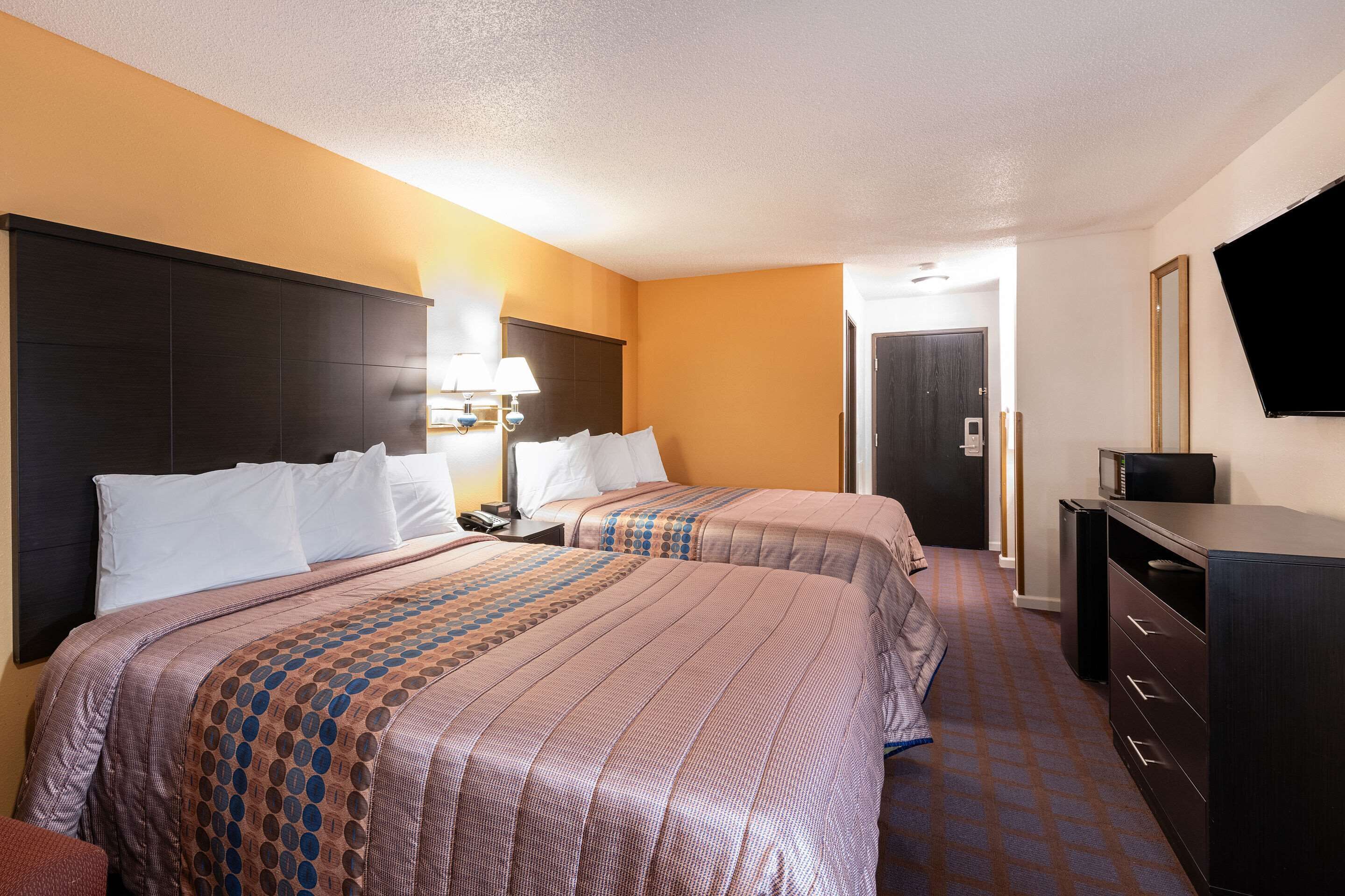 A hotel room with two beds, a TV, a desk with a lamp, and a dresser.