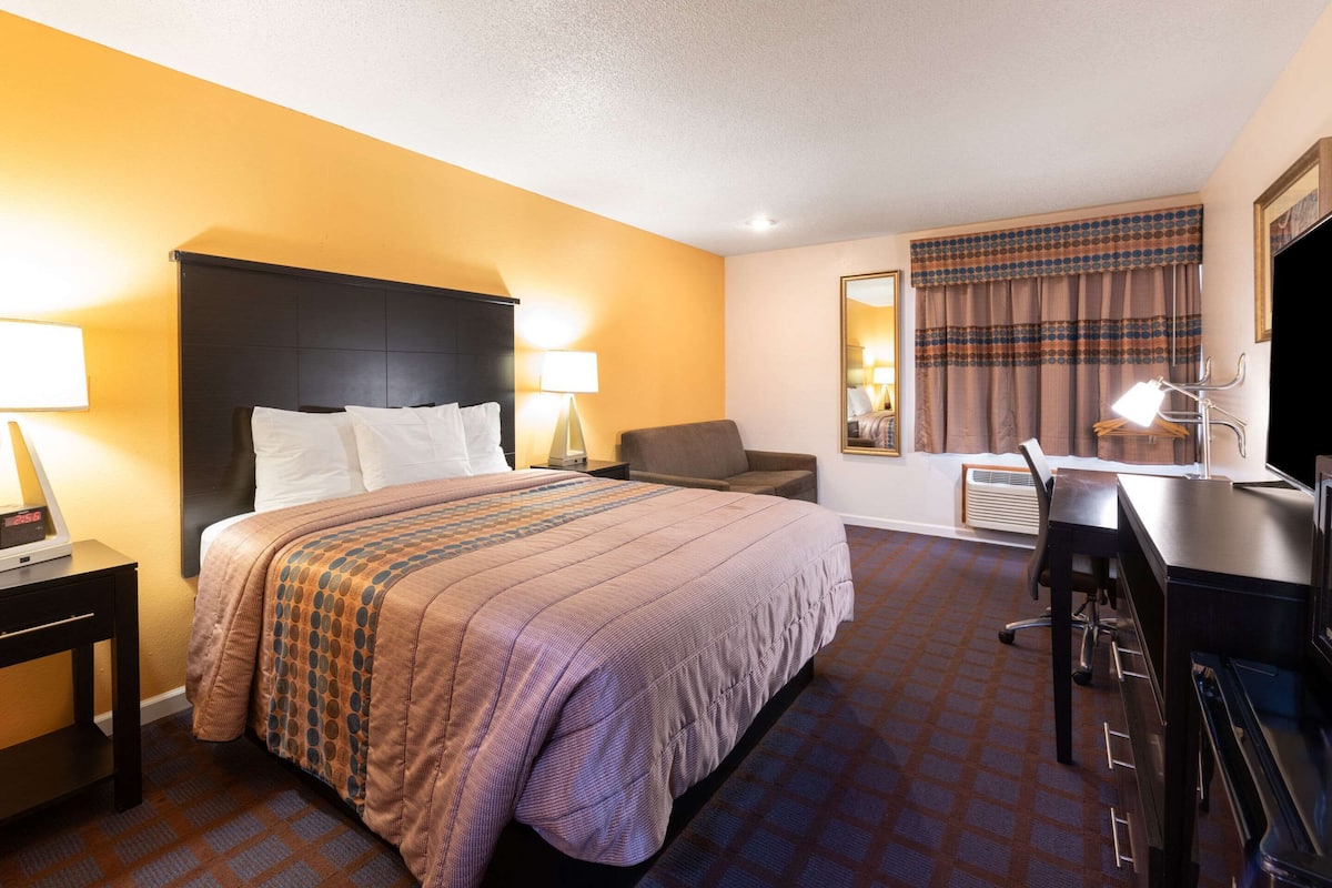 A hotel room with a bed, desk, chair, and a television.