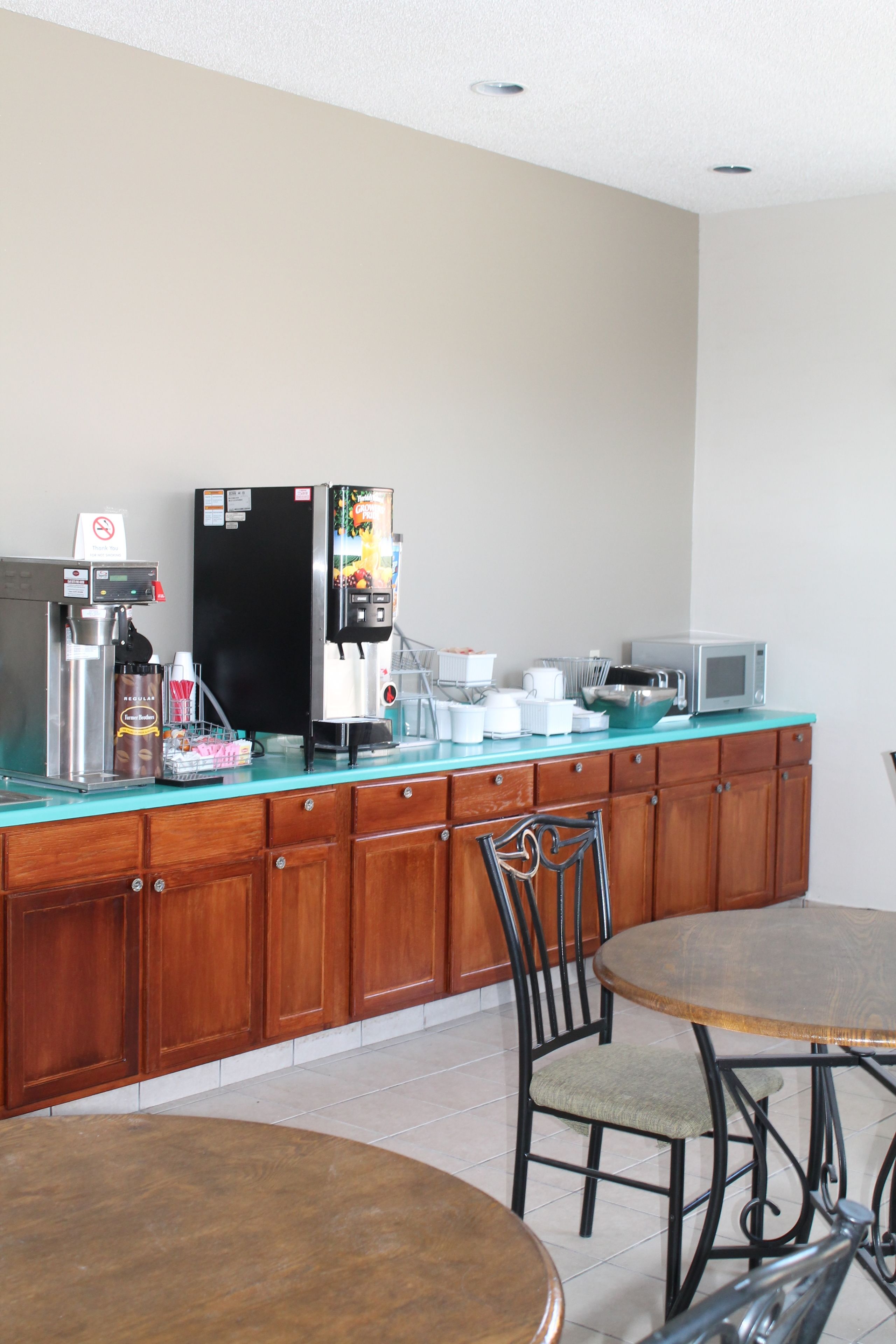 A kitchenette with a coffee machine, microwave, and refrigerator. There is a wooden cabinet and a chair.