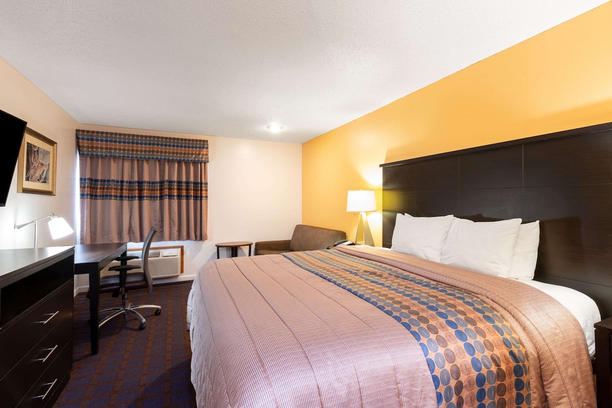 A hotel room with a bed, desk, chair, and a lamp.