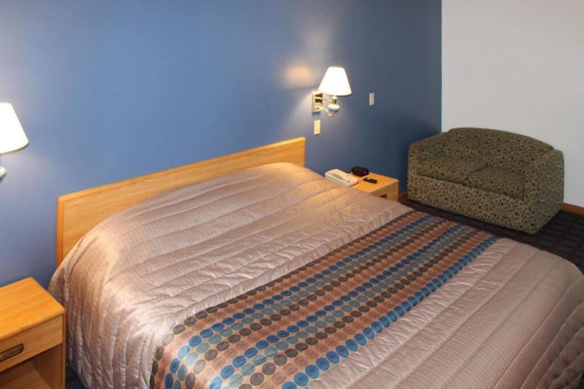 A hotel room with a bed, a nightstand, a lamp, and a chair.