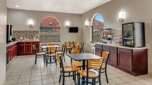 A hotel dining area with a kitchen counter, a TV, and several tables and chairs. - Rodeway Inn Red Oak (Red Oak)