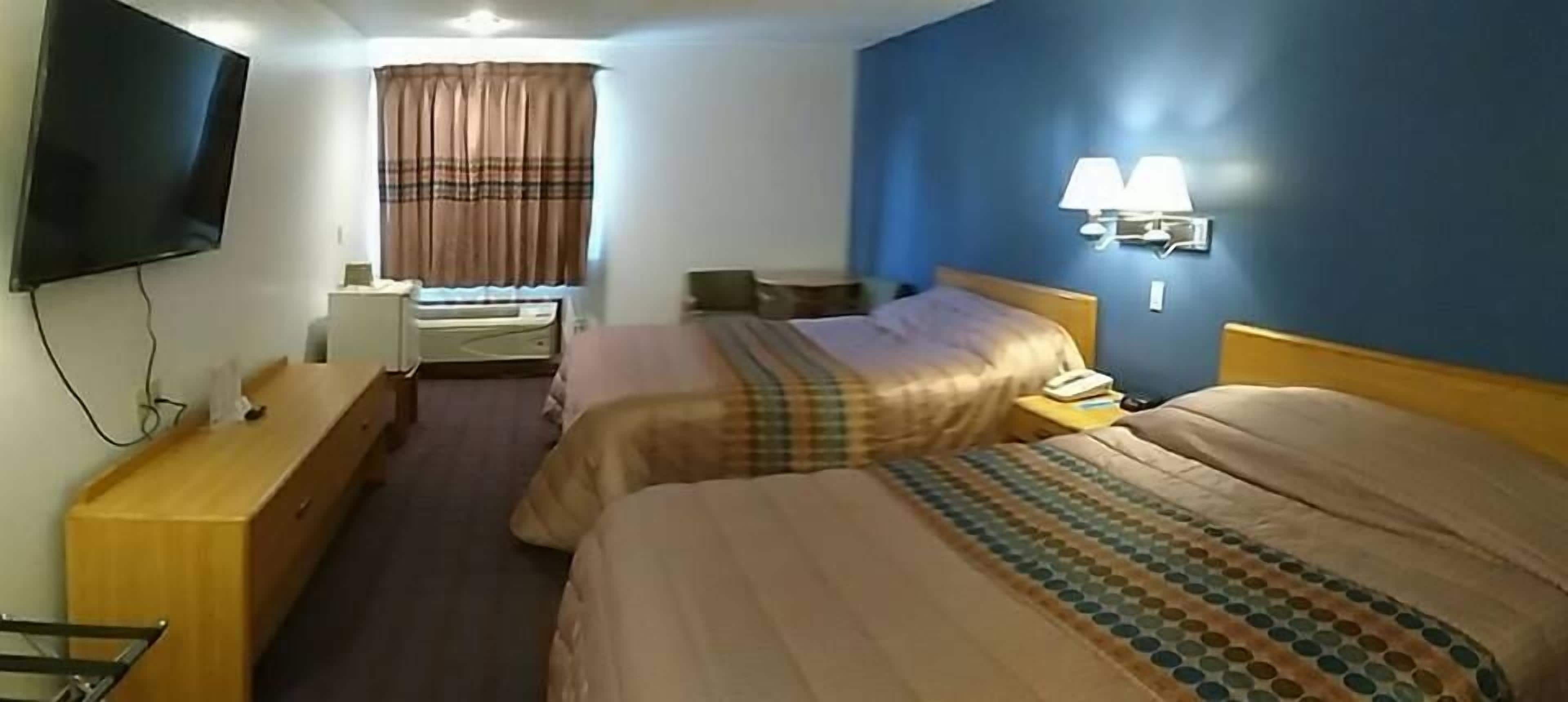 Une chambre d’hôtel avec deux lits, une télévision, un bureau et une fenêtre avec des rideaux.