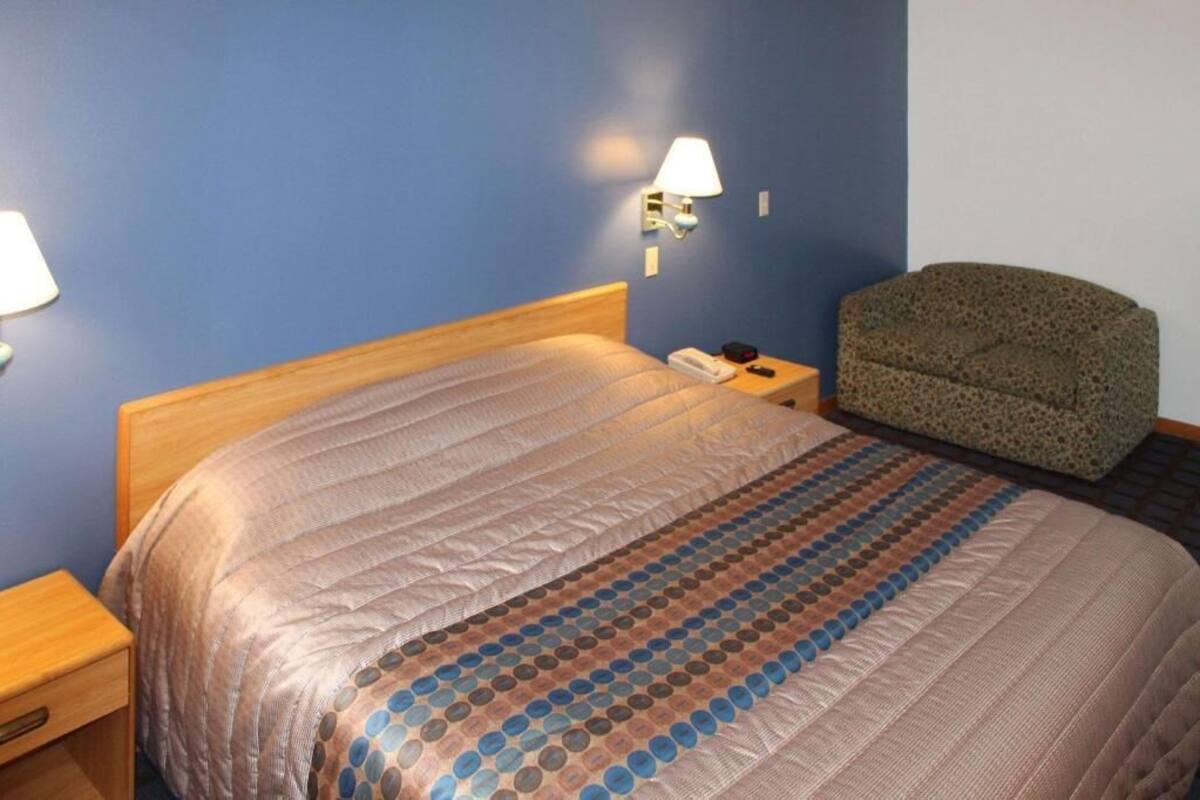 A hotel room with a bed, a nightstand, a lamp, and a chair.