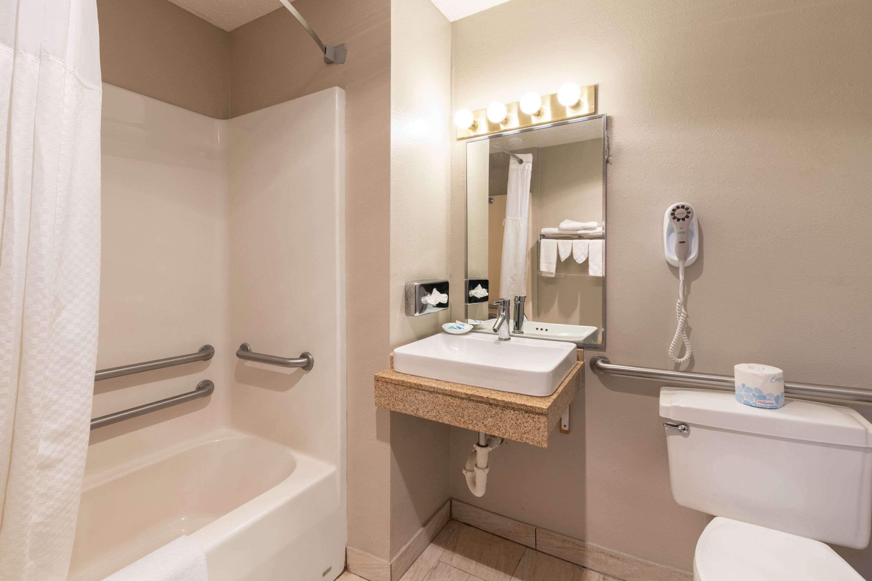 A bathroom with a bathtub, a sink, a toilet, and a mirror with lights above it.