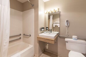 A bathroom with a bathtub, a sink, a toilet, and a mirror with lights above it.