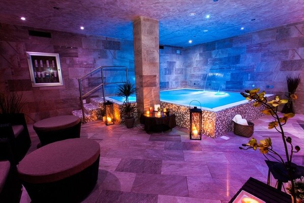 A spa area with a pool, stone walls, seating, and ambient lighting.