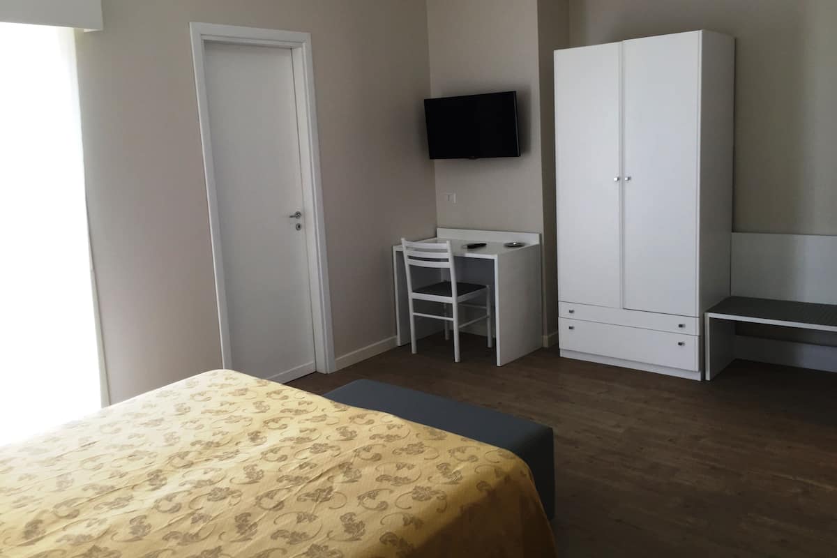 A bedroom with a bed, a desk, a chair, a wardrobe, and a television.