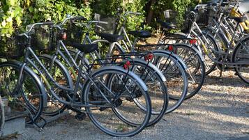 Varias bicicletas estacionadas sobre una superficie de grava, probablemente en un parque o área al aire libre con árboles y follaje de fondo.