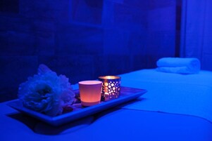 Un ambiente de spa con una bandeja de flores y velas sobre una mesa, una toalla y un muro de piedra al fondo.