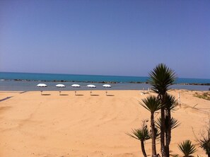 A sandy beach with four white umbrellas and palm trees. - Hotel Costazzurra Museum & Spa (Agrigento)