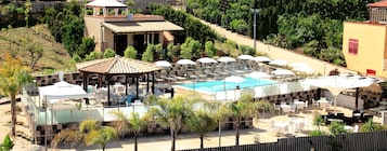 Un área de piscina en la azotea con tumbonas y sombrillas, rodeada de follaje y un pequeño pabellón.