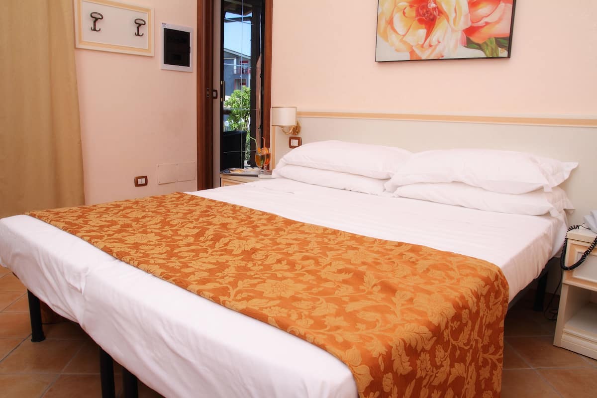 A neatly made bed with a patterned bedspread, a bedside table with a lamp, and a wall-mounted painting.