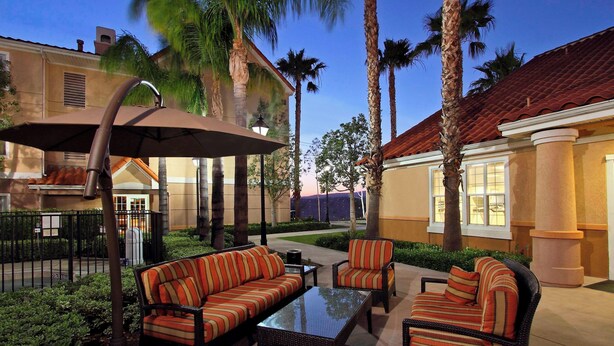 A patio area with outdoor furniture, palm trees, and a building with a red-tiled roof. - Residence Inn Anaheim Hills Yorba Linda (Anaheim)