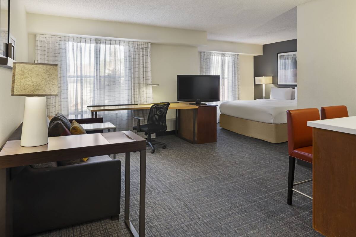 A hotel room with a bed, desk, television, and seating area.