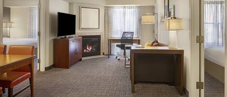 Una habitación de hotel con chimenea, televisión, escritorio y cama.