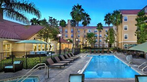 Ein Hotelpoolbereich mit Liegestühlen, einem Schwimmbecken und einem Gebäude mit mehreren Balkonen.