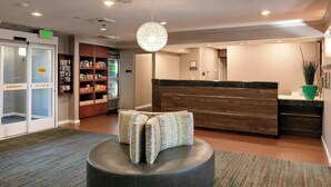 A lobby with a reception desk, a waiting area with a round ottoman, a vending machine, and a large decorative light fixture. - Residence Inn Anaheim Hills Yorba Linda (Anaheim)