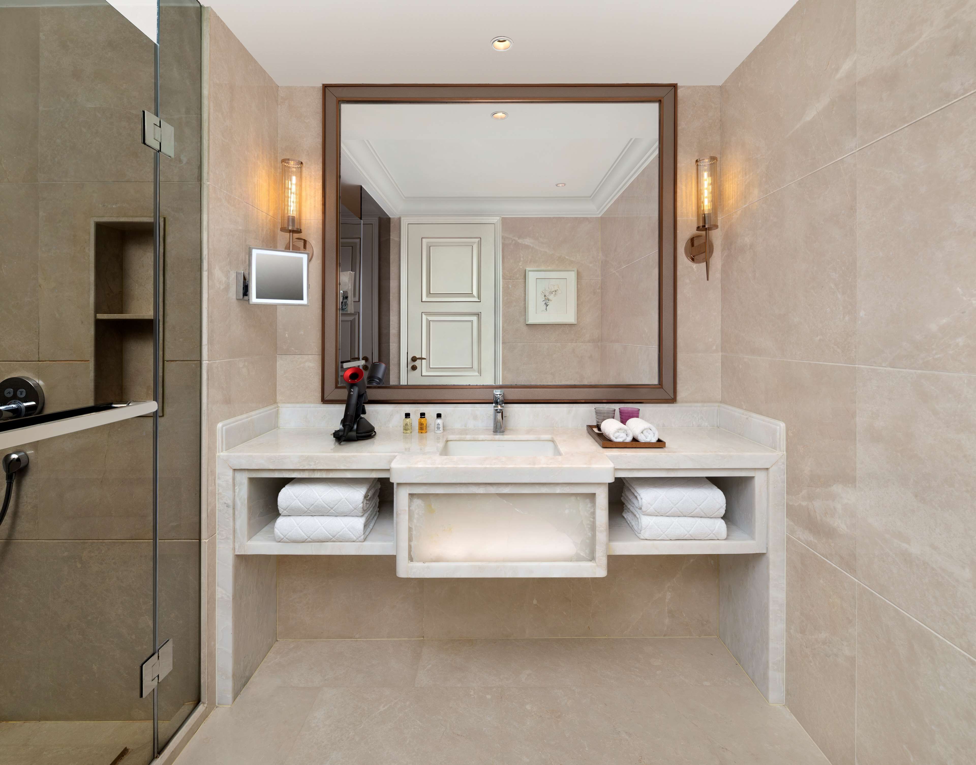 A modern bathroom with a large mirror, two sinks, a shower, and a towel rack.