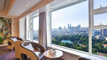 Una habitación de hotel moderna con ventanas amplias que ofrecen vistas a la ciudad, un área de descanso acogedora y una estantería.