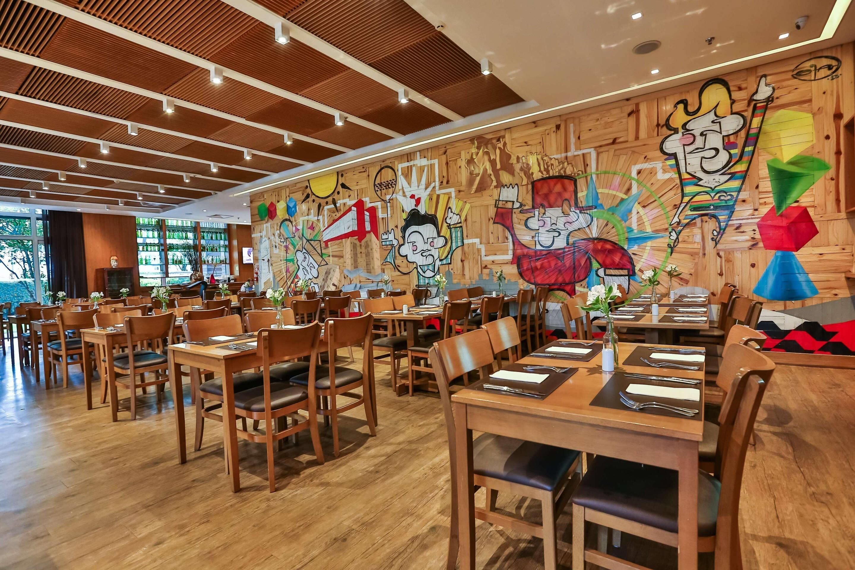 Un restaurante con mesas y sillas de madera, techo de madera y coloridos adornos murales.