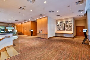 Um lobby moderno de hotel, com um balcão de recepção, uma parede de quadros e piso coberto de carpete.