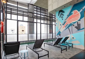 A modern interior with large windows, lounge chairs, and a colorful mural.