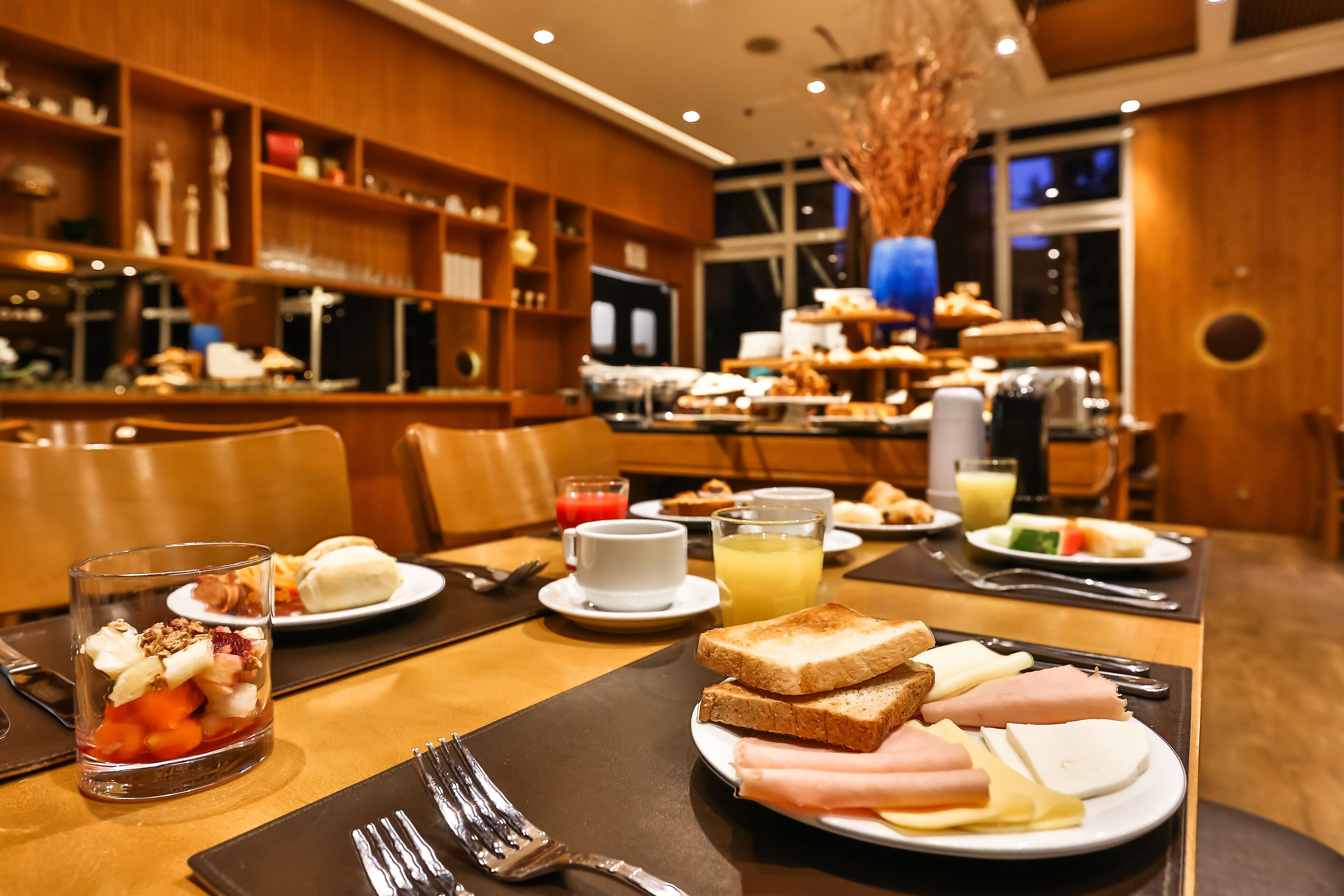 Mesa de café da manhã com diversos alimentos em pratos, como torradas, queijo e frios.