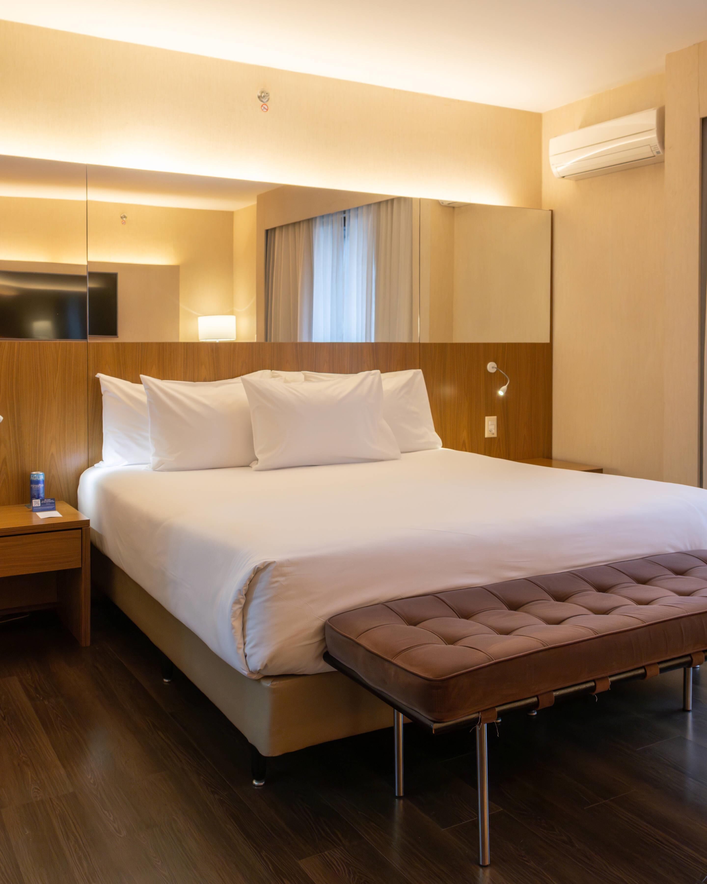 Una camera d'albergo con un letto grande, una testiera in legno, un comodino con una lampada e un condizionatore d'aria a parete.