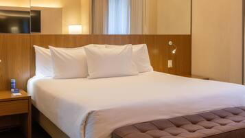 Una camera d'albergo con un letto grande, una testiera in legno, un comodino con una lampada e un condizionatore d'aria a parete.