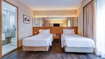 Ett hotellrum med två sängar, en sänggavel i trä, ett nattduksbord med en telefon och en stor spegel.