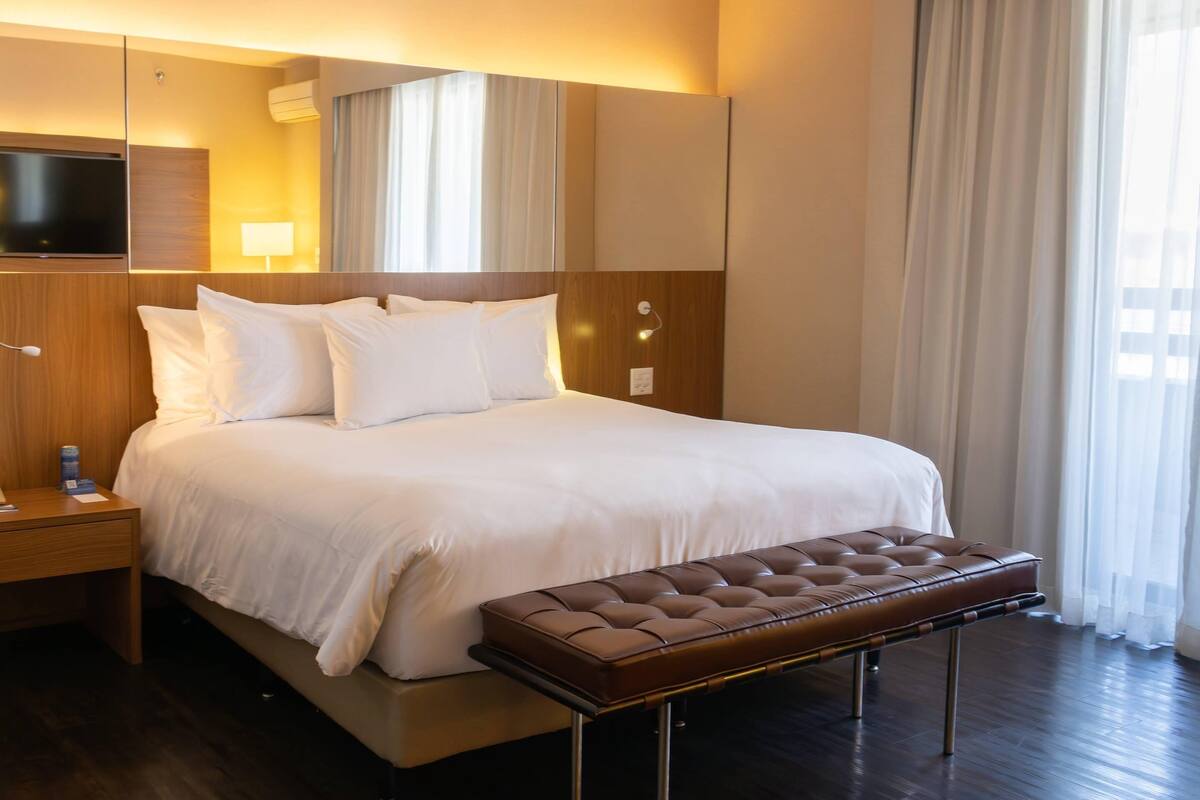 A hotel room with a large bed, a flat-screen TV, a bedside table, and a window with curtains.