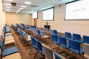 A conference room with rows of chairs, a projector screen, and a presentation screen.