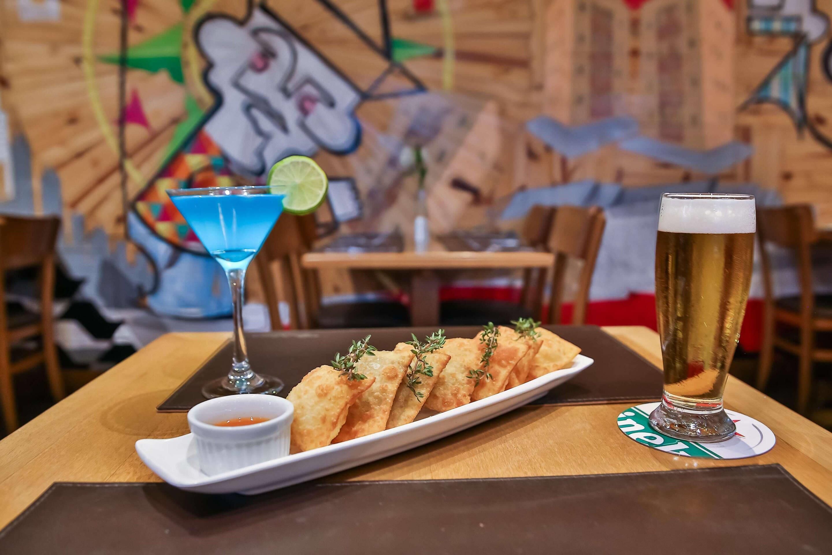 Una mesa con un plato de comida frita, una copa de martini y un vaso de cerveza grande.