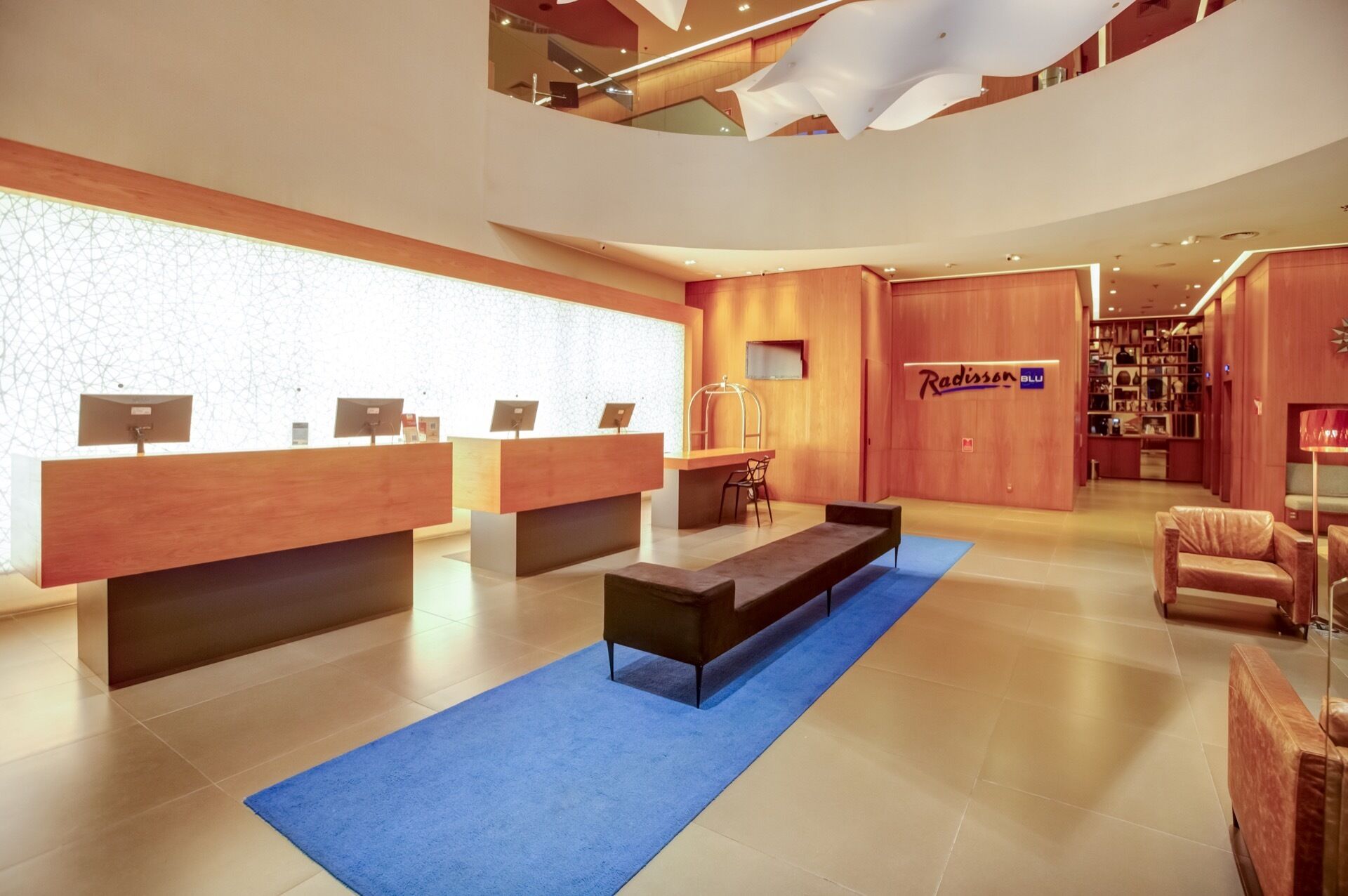 A modern reception area with wooden reception desks, a blue carpet, and a Radisson BLU sign.