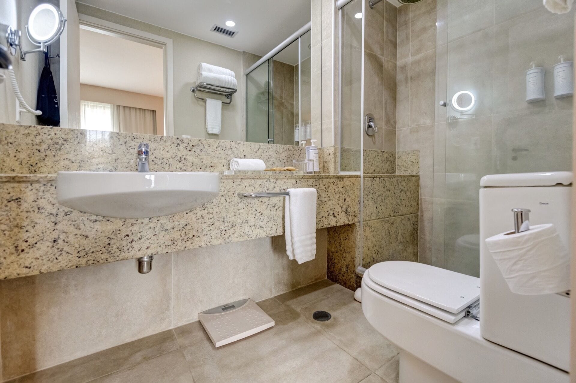 Un baño moderno con lavamanos de granito, cabina de ducha con vidrio y un inodoro.