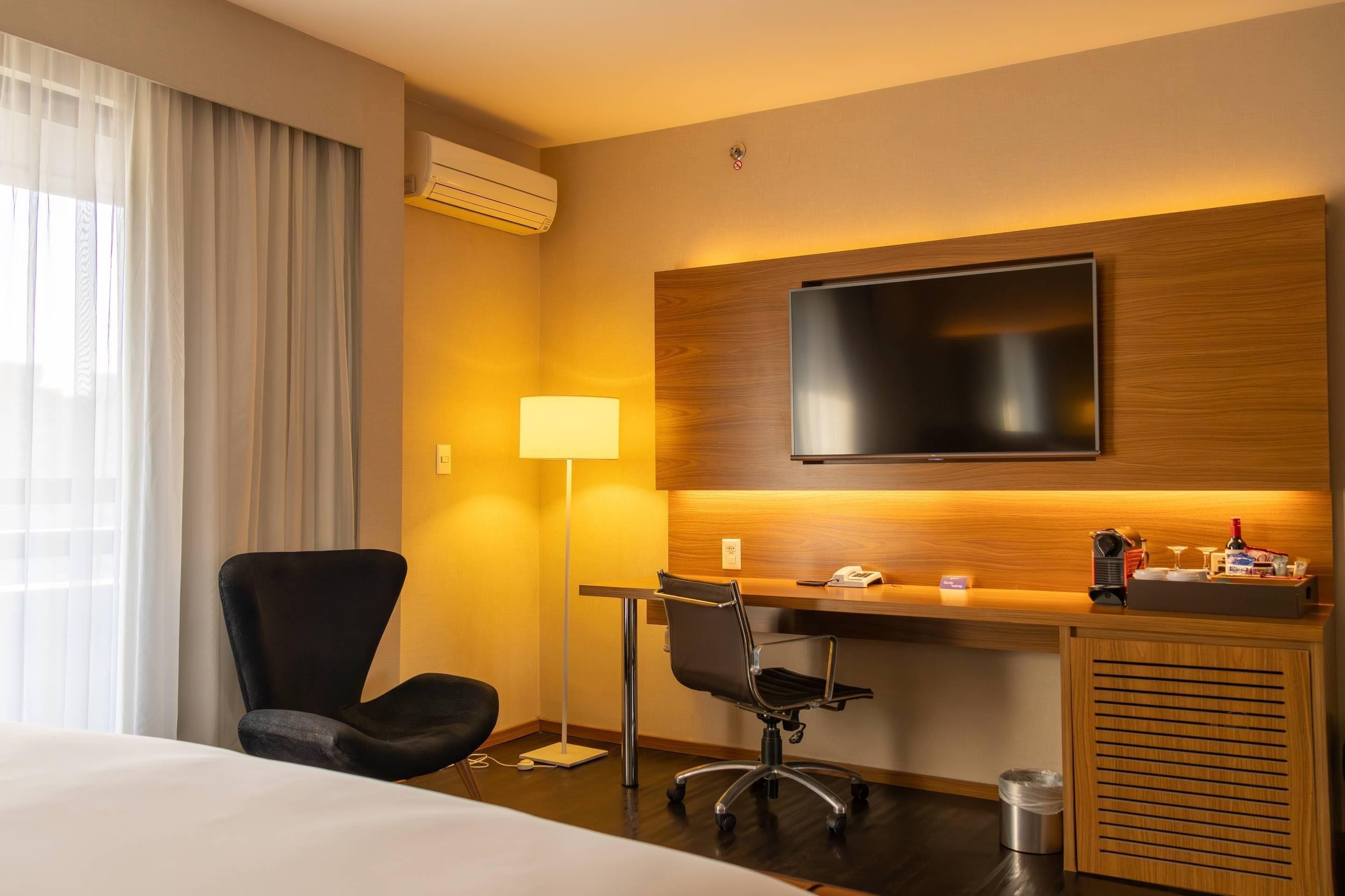 A hotel room with a bed, a desk with a chair, a television, and a lamp.