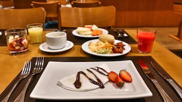 A breakfast setting with a plate of pancakes, strawberries, and chocolate sauce, a glass of orange juice, and a plate of eggs and bacon.