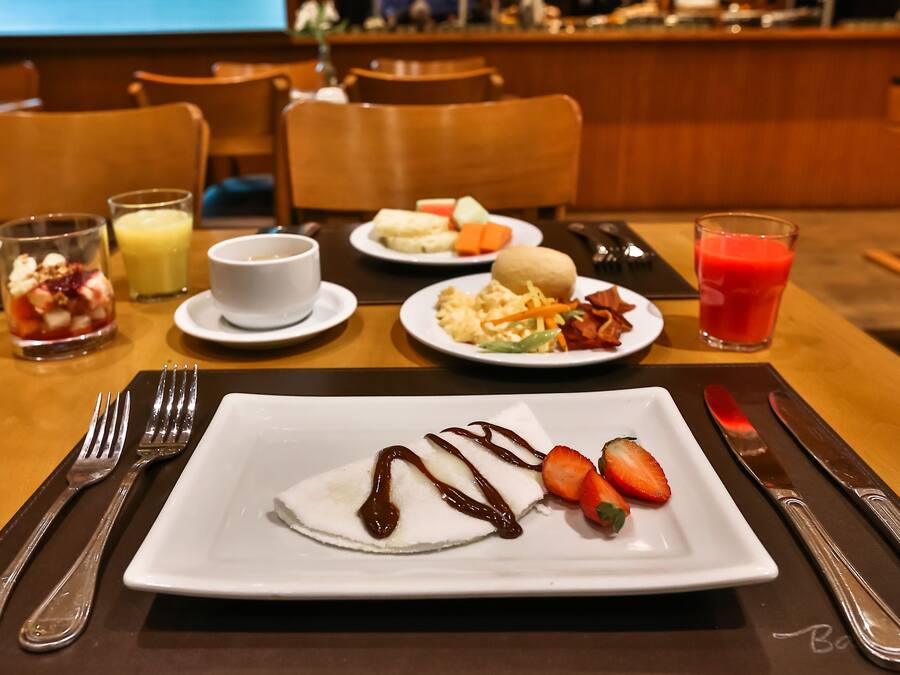 A breakfast setting with a plate of pancakes, strawberries, and chocolate sauce, a glass of orange juice, and a plate of eggs and bacon.
