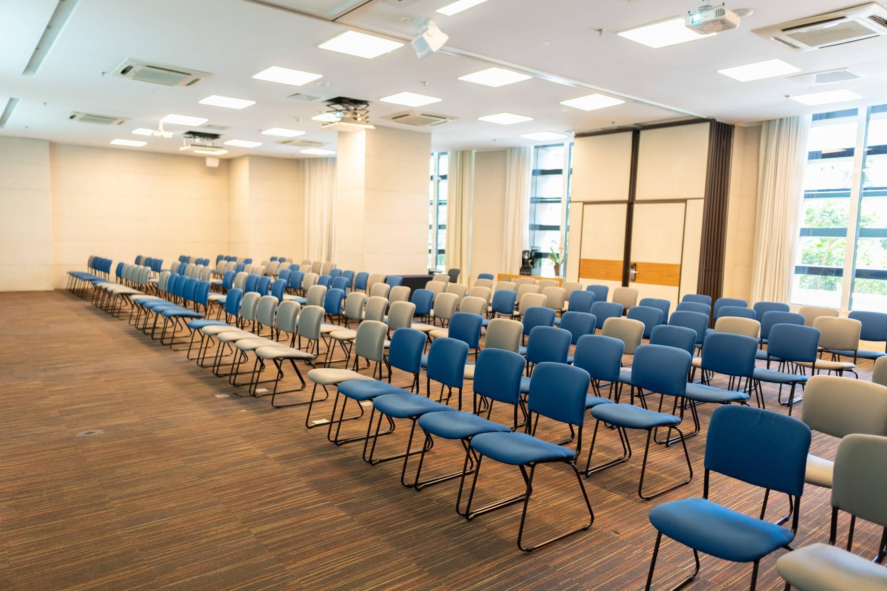 A conference room with rows of chairs, large windows, and a projector screen.